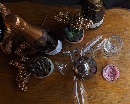 Bottle of champagne, wine glasses, and a small plant on a wooden table.